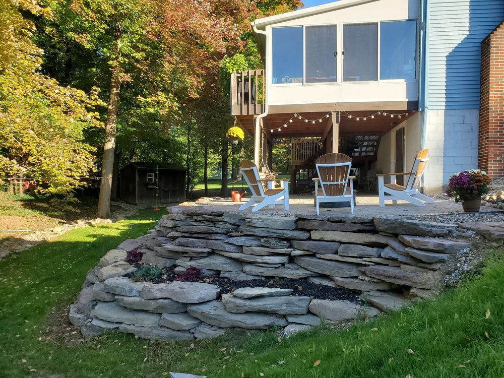 Stacked flagstone outcropping wall terracing up to a patio with Adirondack chairs