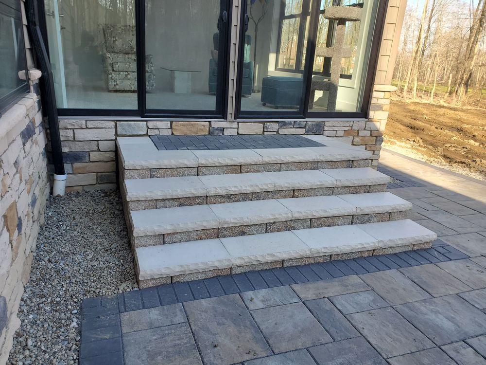 Wide natural stone slab steps up to a slider on a large-format paver terrace