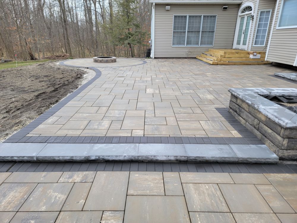 Large paver terrace with a circular fire pit inset against the woods