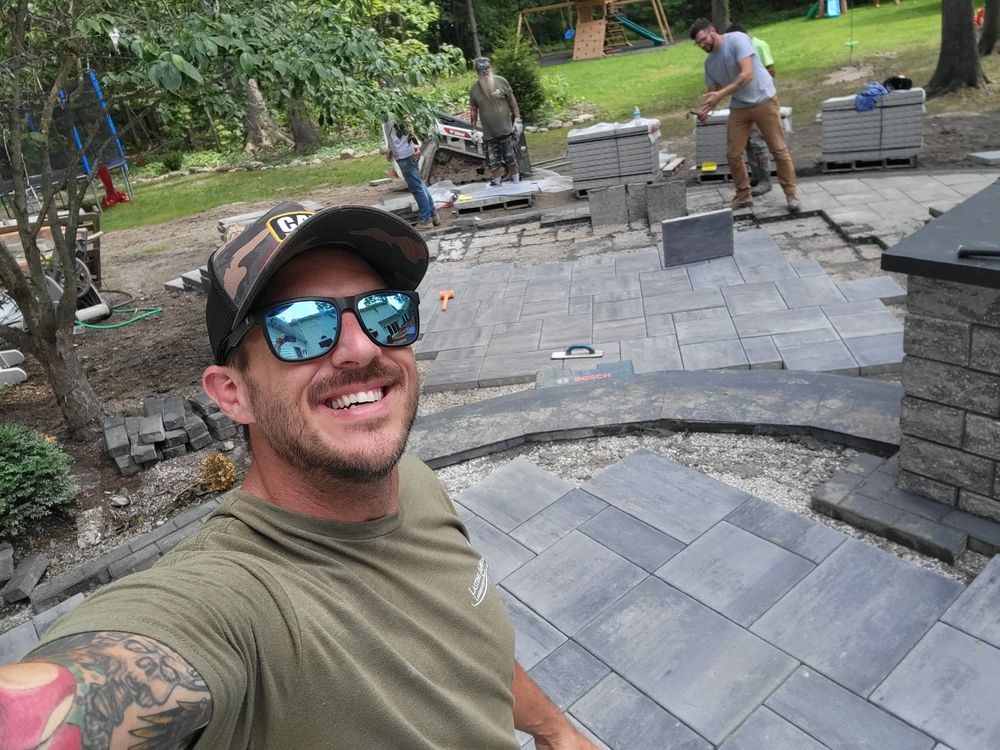 Marcus Peters on a Lasting Impressions job site with the crew laying a paver patio behind him