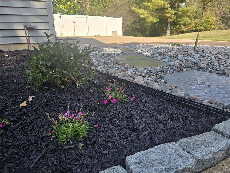 Dry creek bed of river rock with flat stepping stones through it beside planted beds