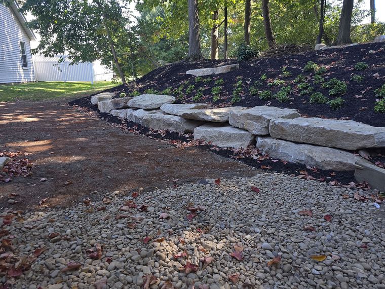 Boulder outcropping retaining a mulched slope with a river rock swale running below it