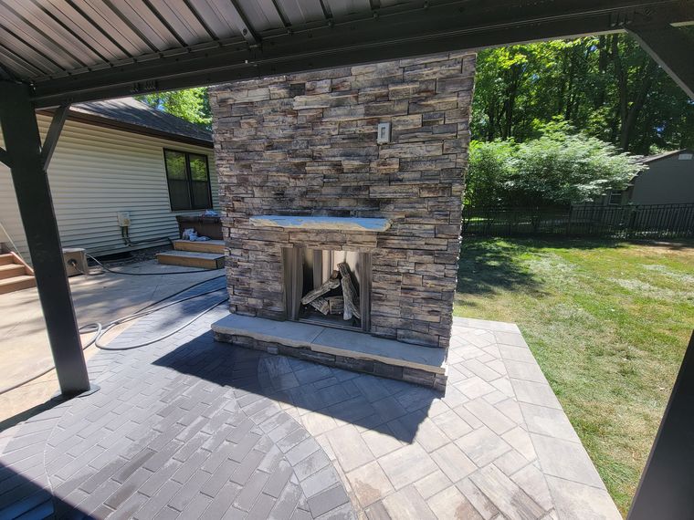 Outdoor fireplace with a heavy stone mantel over a herringbone paver field