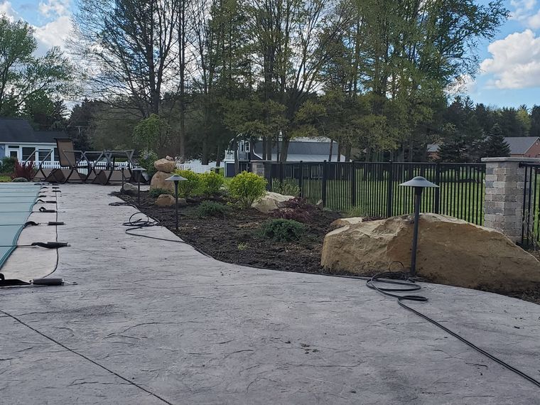 Stamped concrete pool deck with path lights in, a boulder accent and block pillars