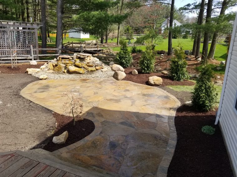 Irregular flagstone patio sweeping to a boulder waterfall with new plantings