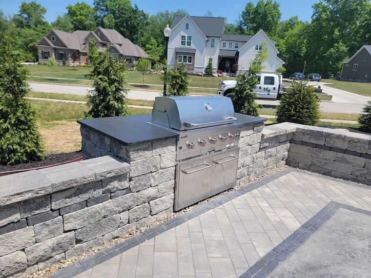 Stone-veneered grill island with a dark stone countertop and built-in grill