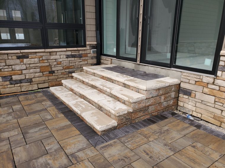 Large-format paver patio with a charcoal border and wide stone slab steps up to the sliders