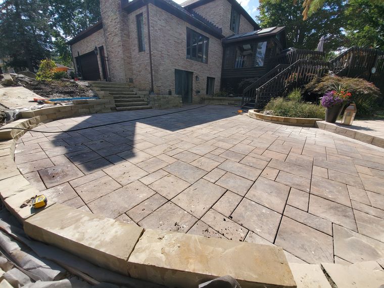 Multi-level paver terrace with sandstone block seat walls and steps behind a brick house