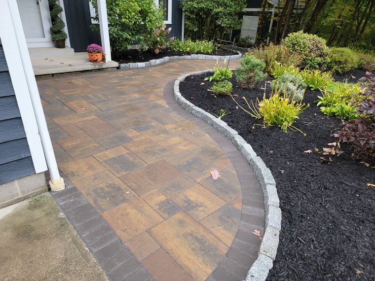 Paver walk with a curved granite cobble border and a black mulch bed of mixed perennials