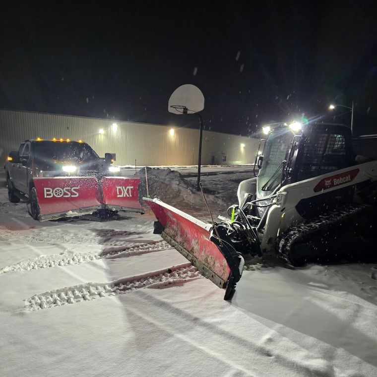 Night plowing in falling snow with a BOSS plow truck and a track loader working a lot