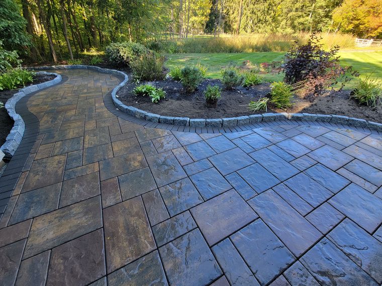 Paver walk with a cobble border sweeping around a planted bed with autumn woods behind